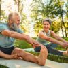 senior man and woman stretch their legs on yoga mats outside